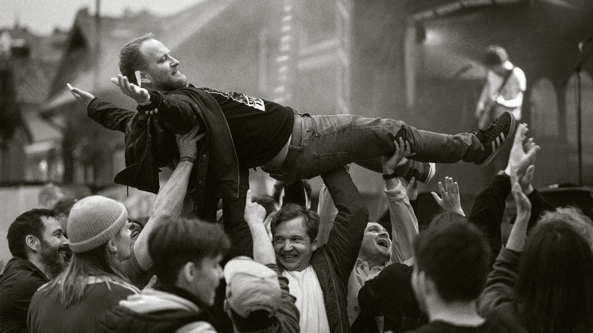 En mann bæres over hodene på publikum under en konsert. Svart-hvitt.